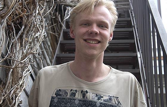 Josh standing in front of staircase covered on one side with vines. 微笑着，金色的头发