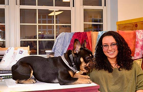 Simone sits to the left, with  small dog sitting on table to her right